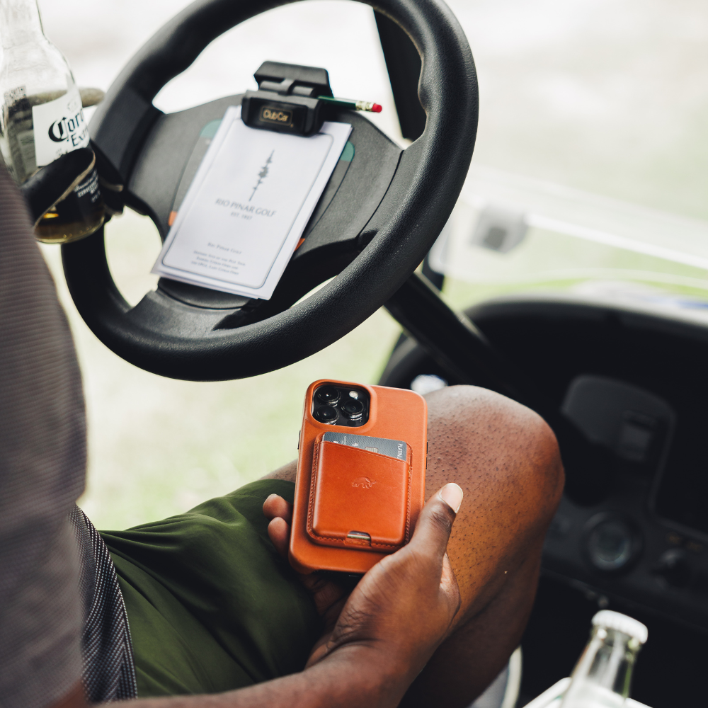 Brown magnetic card wallet on phone in hand in golf cart; steering wheel shows RIO PINAR GOLF, Club Car clip, Corona Extra