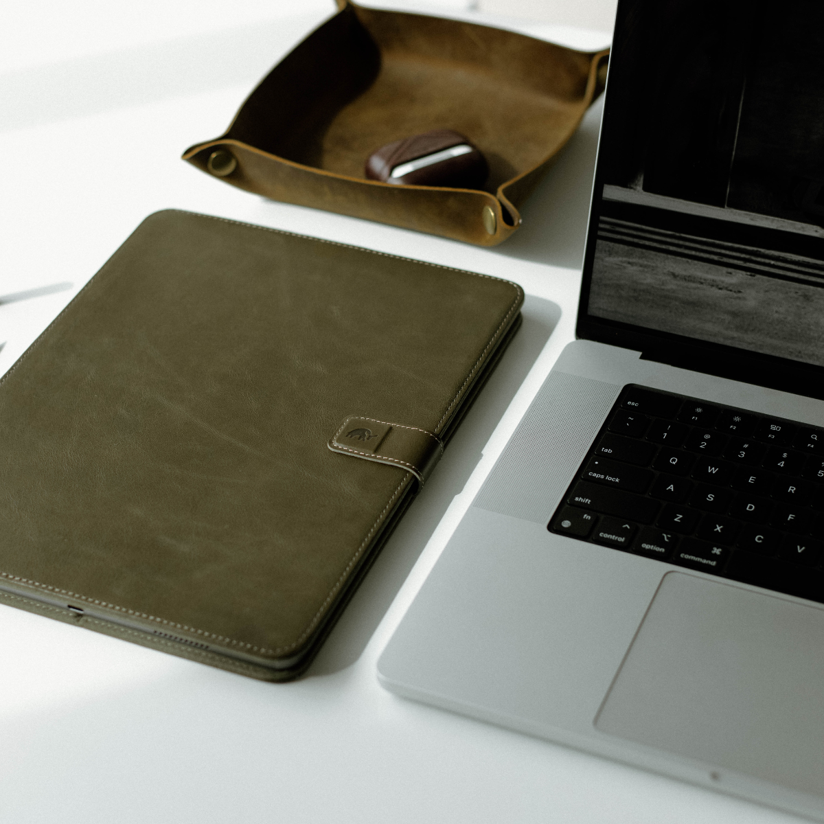 Minimalist leather iPad case in olive green on a desk next to a laptop and tray