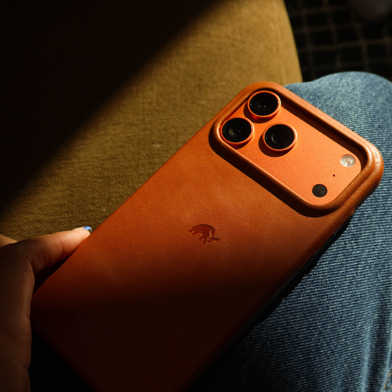 Angled back view of sienna leather Contemporary Plateau iPhone case showing raised camera plateau and embossed logo on denim
