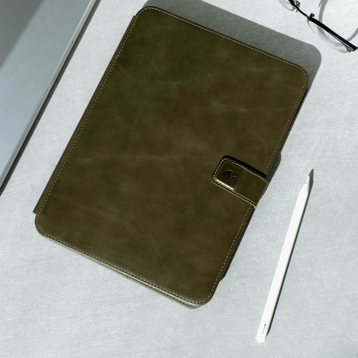 Dark green leather iPad case with a clasp and a stylus beside it