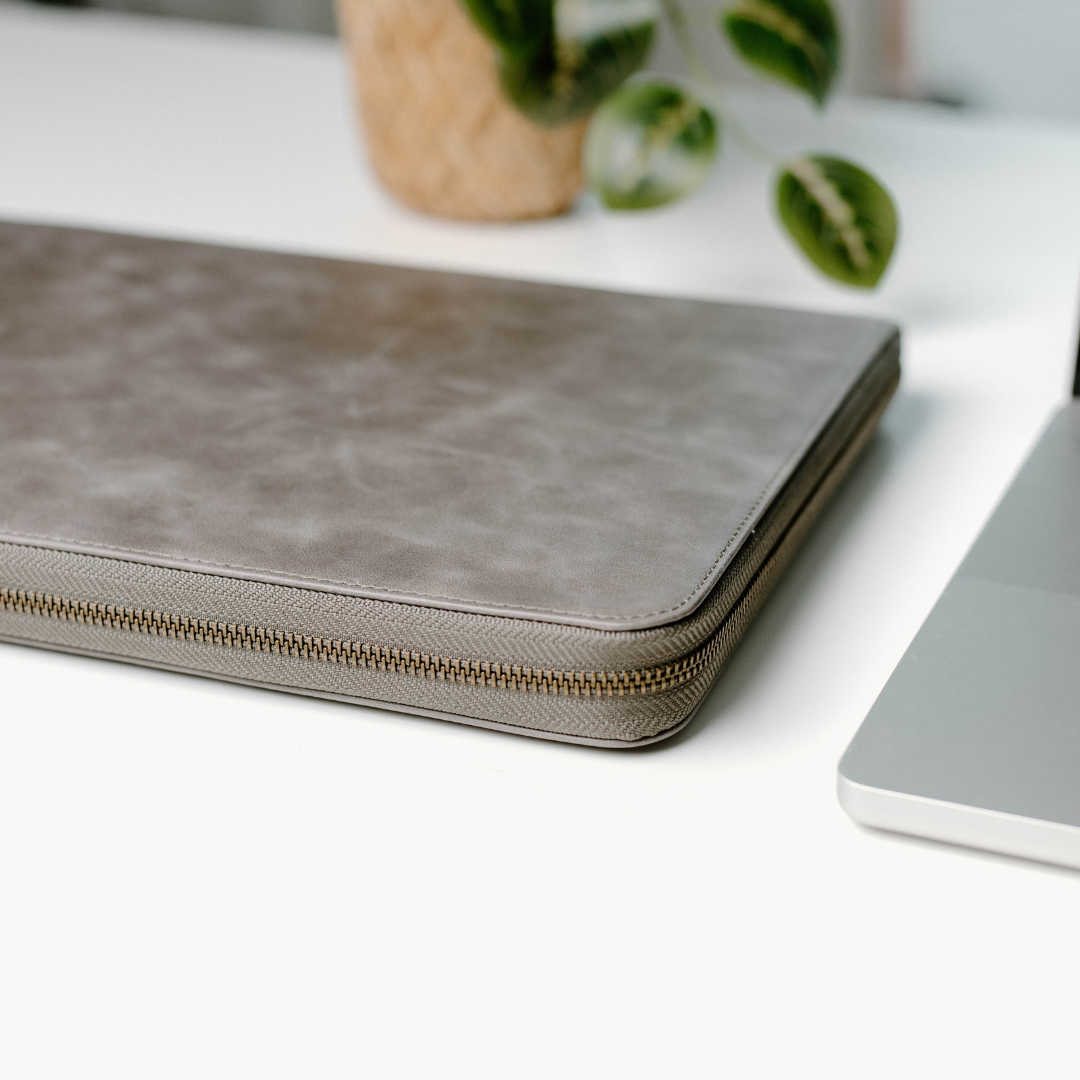 Leather MacBook Sleeve in Slate color, featuring a zipper and a sleek design on a desk.