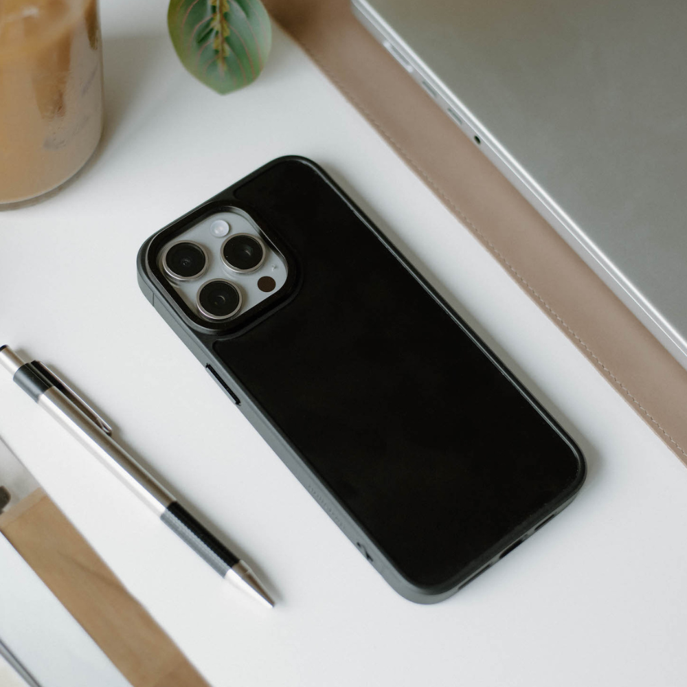 Smartphone with a black protective case lying on a white desk next to a pen and closed laptop