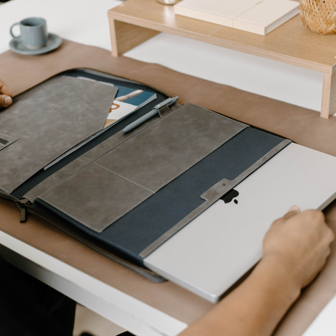 Open leather MacBook sleeve displaying a laptop and accessories on a desk