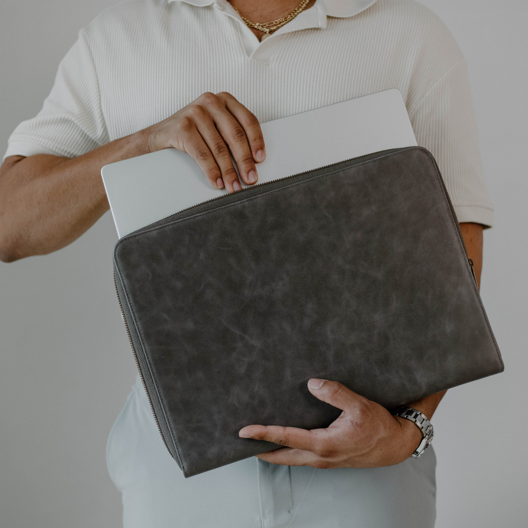 Person holding a gray leather MacBook sleeve with a laptop inside