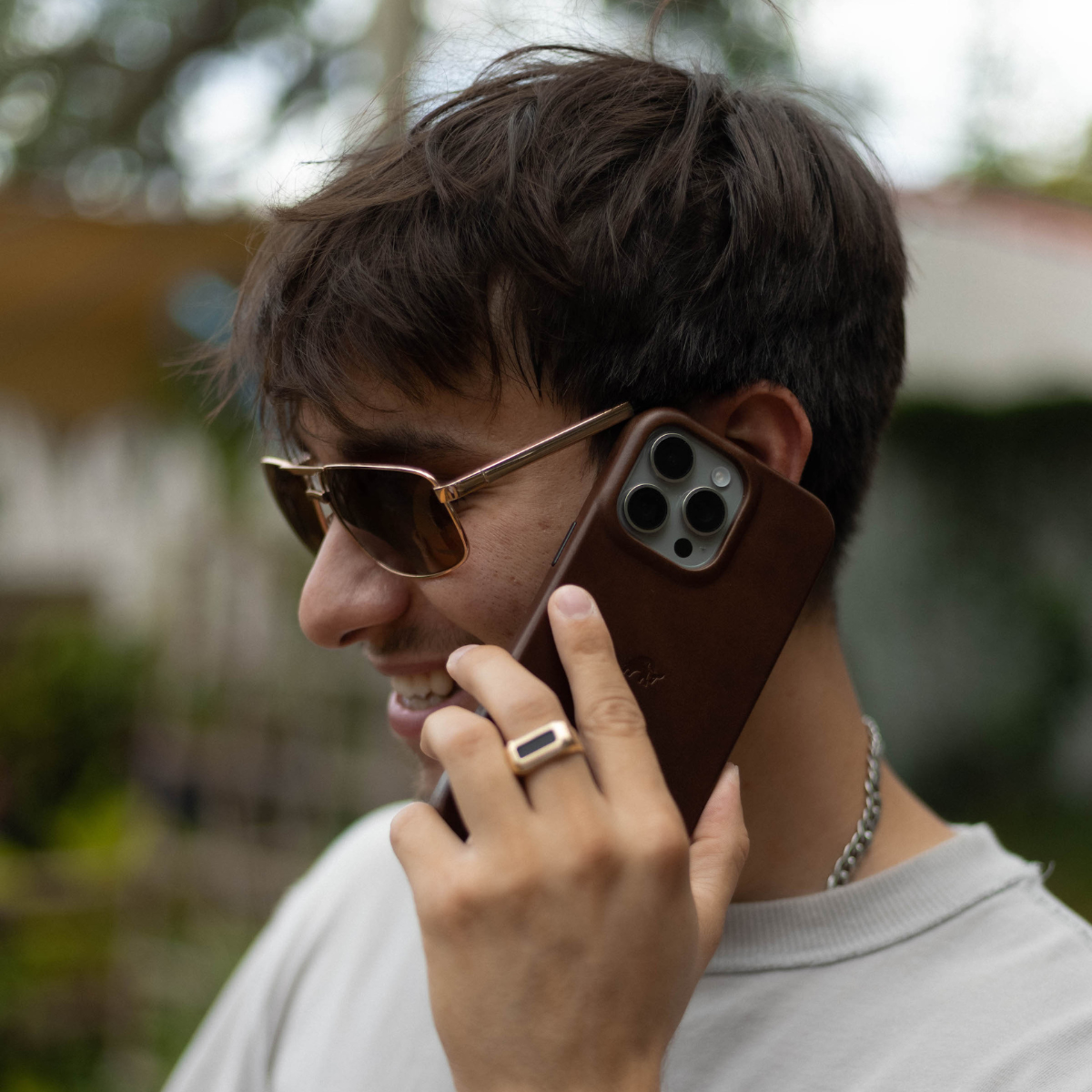 Smiling young man wearing sunglasses holds phone to his ear in a brown leather minimalist case.