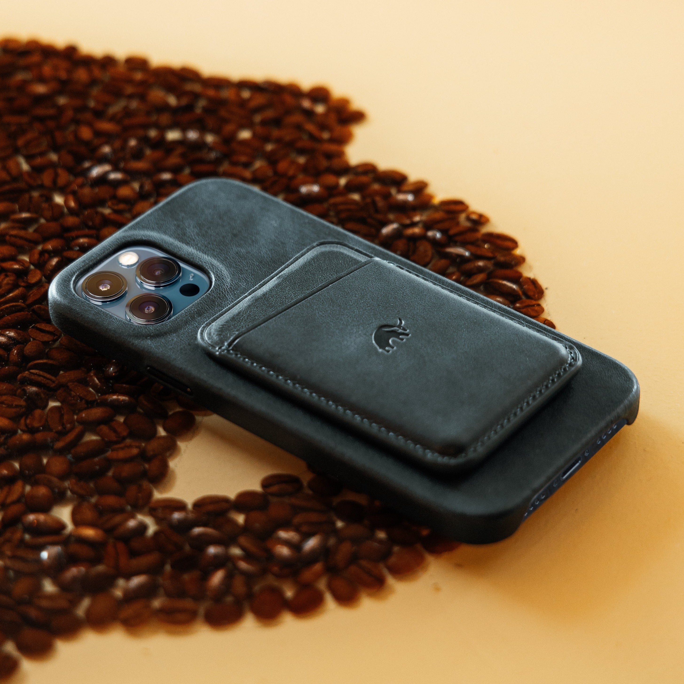 Dark green leather iPhone case with attached magnetic card wallet, resting on scattered coffee beans
