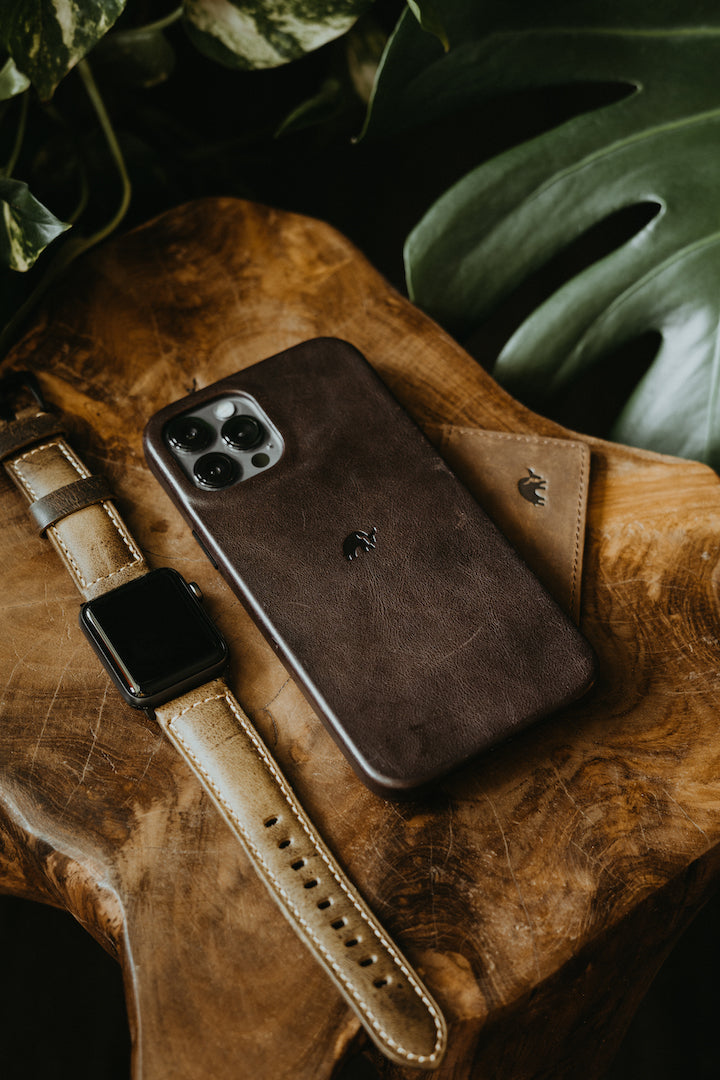 Brown leather phone case, wallet, and watch on a wooden surface