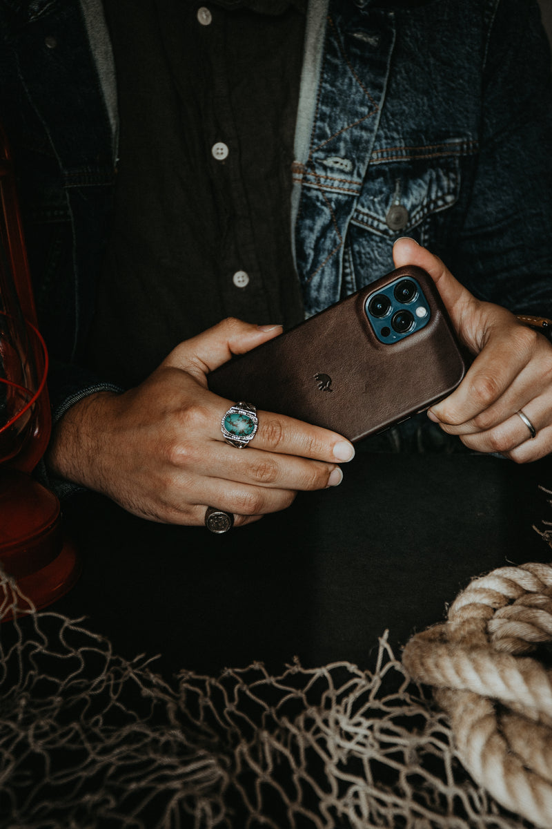 Angled back view of The Minimalist bourbon leather iPhone case showing MagSafe compatibility in a model's hands