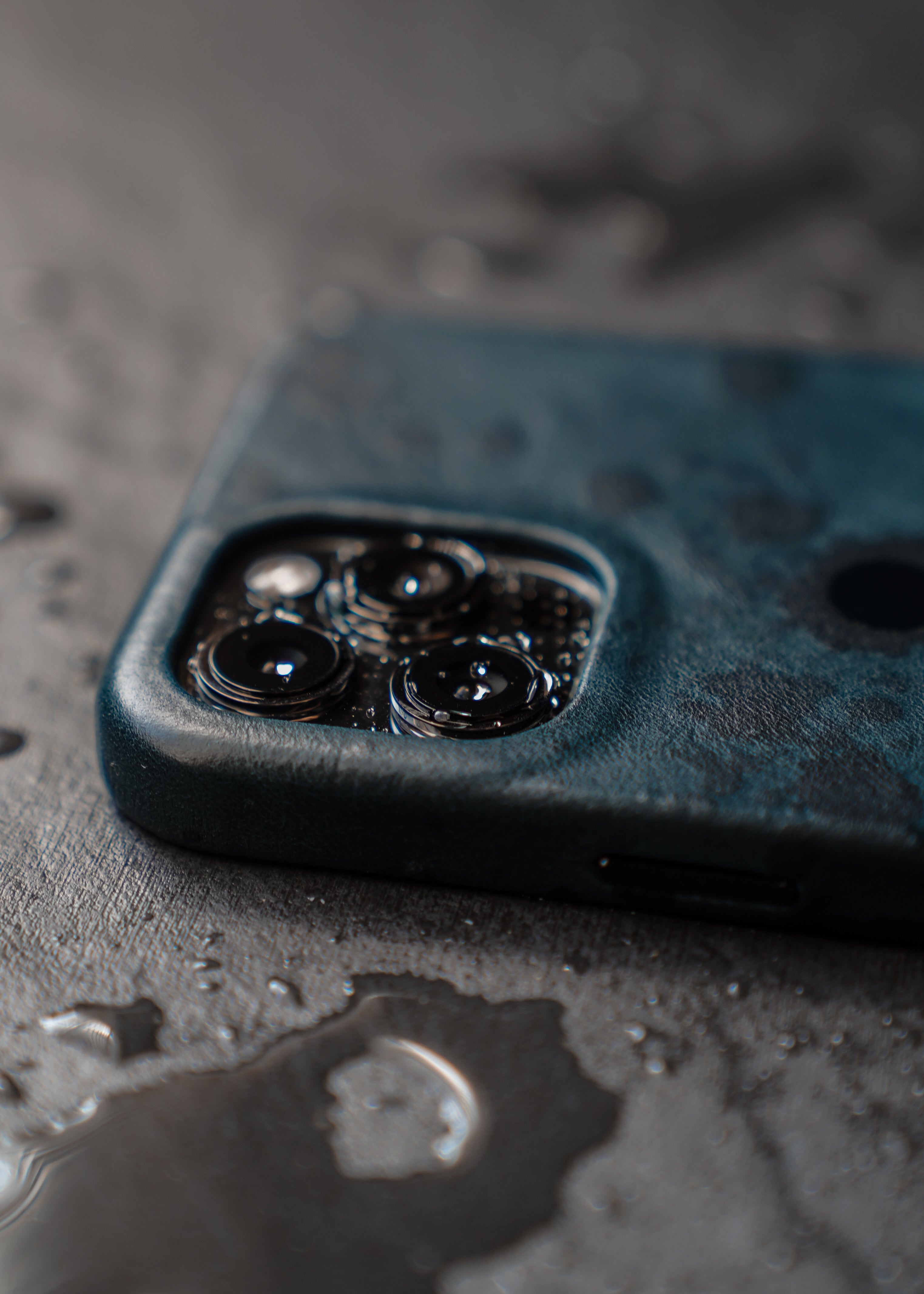 Close-up of a smartphone camera module with three lenses and water droplets on a wet surface.