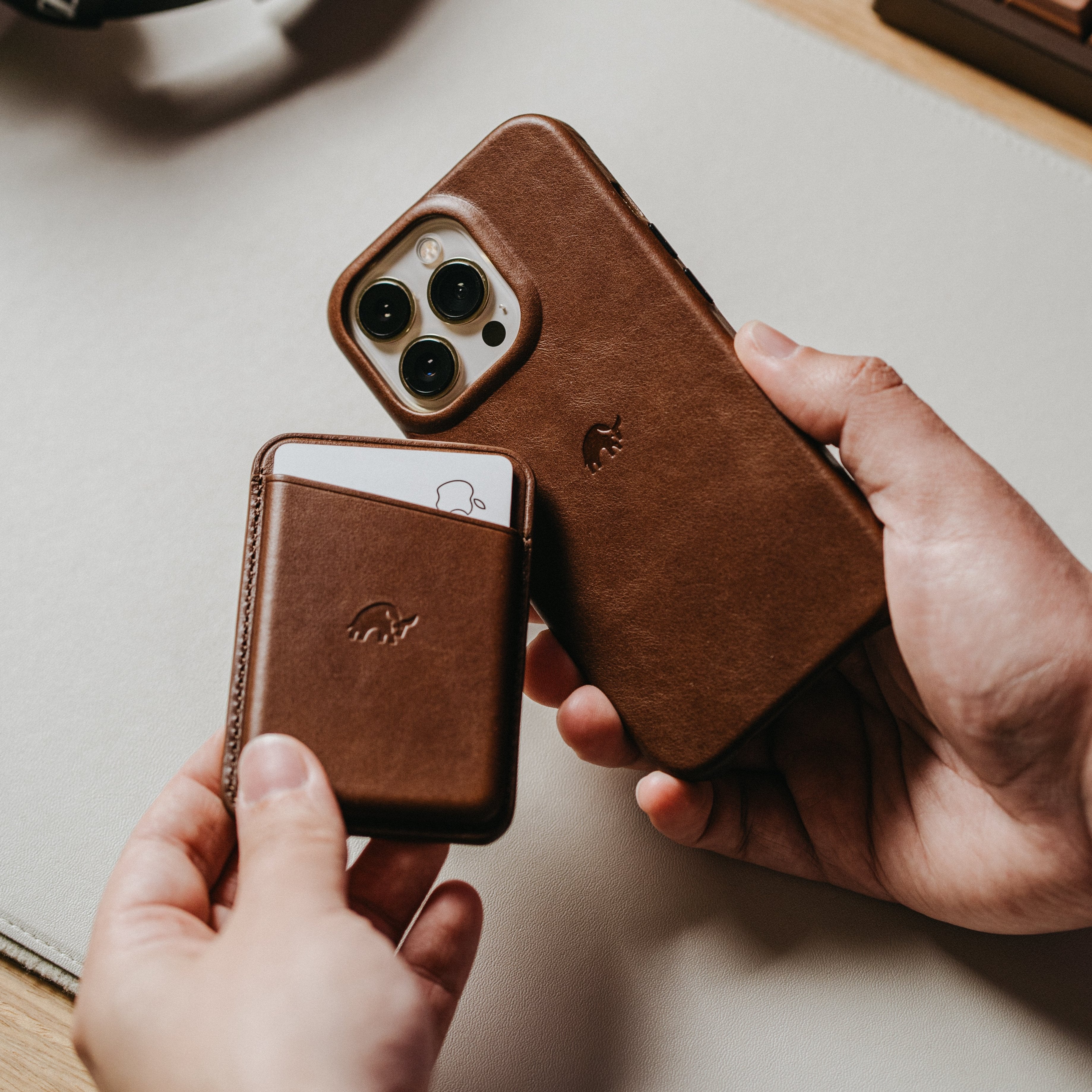 A person holding a brown leather phone case and wallet, both embossed with a logo.