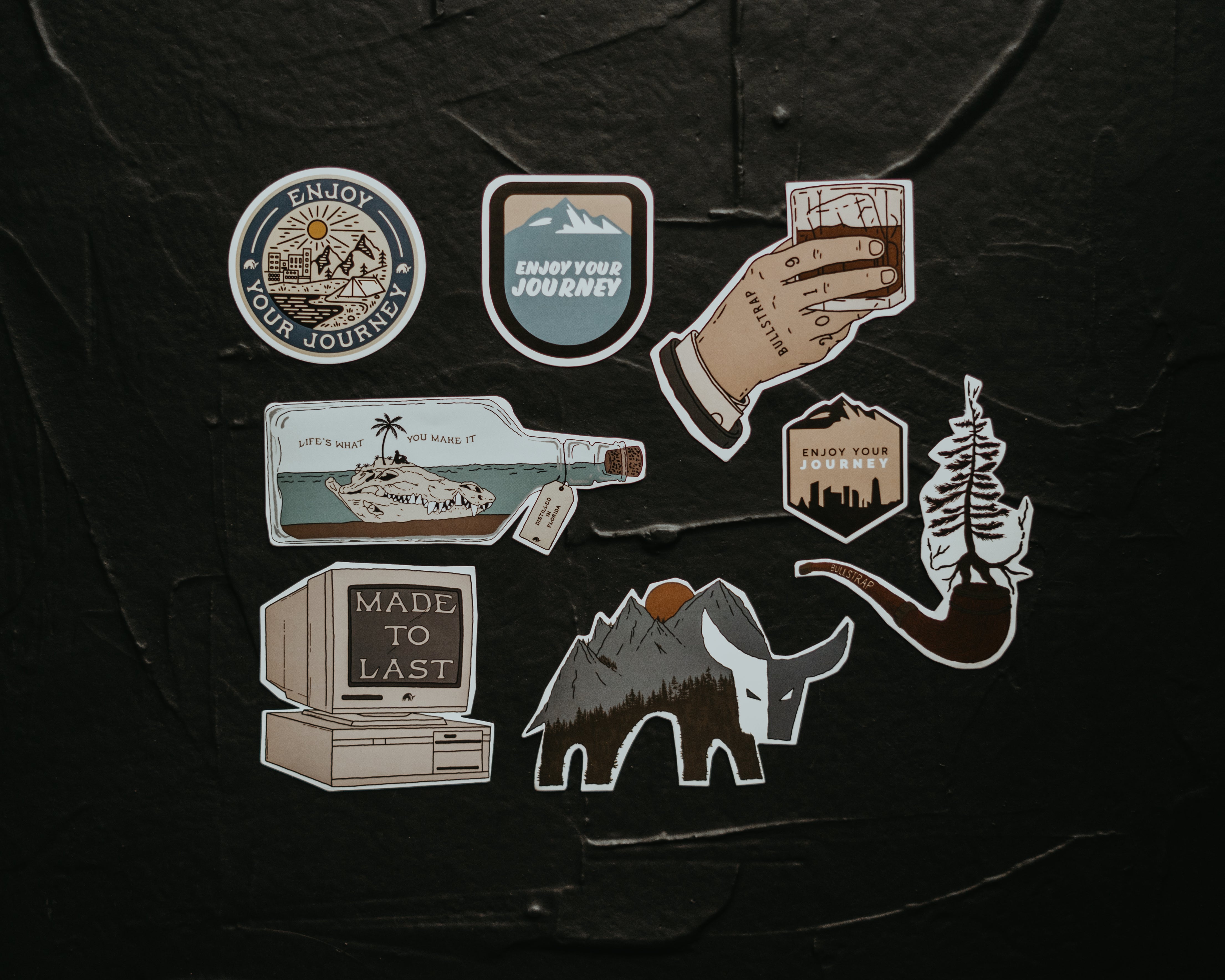 A collection of stickers featuring designs that say 'Enjoy Your Journey', 'Made to Last', and illustrations of mountains and a bottle.