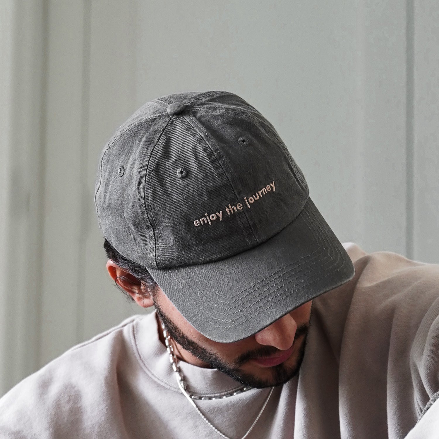 A person wearing a grey hat with the text 'enjoy the journey'.