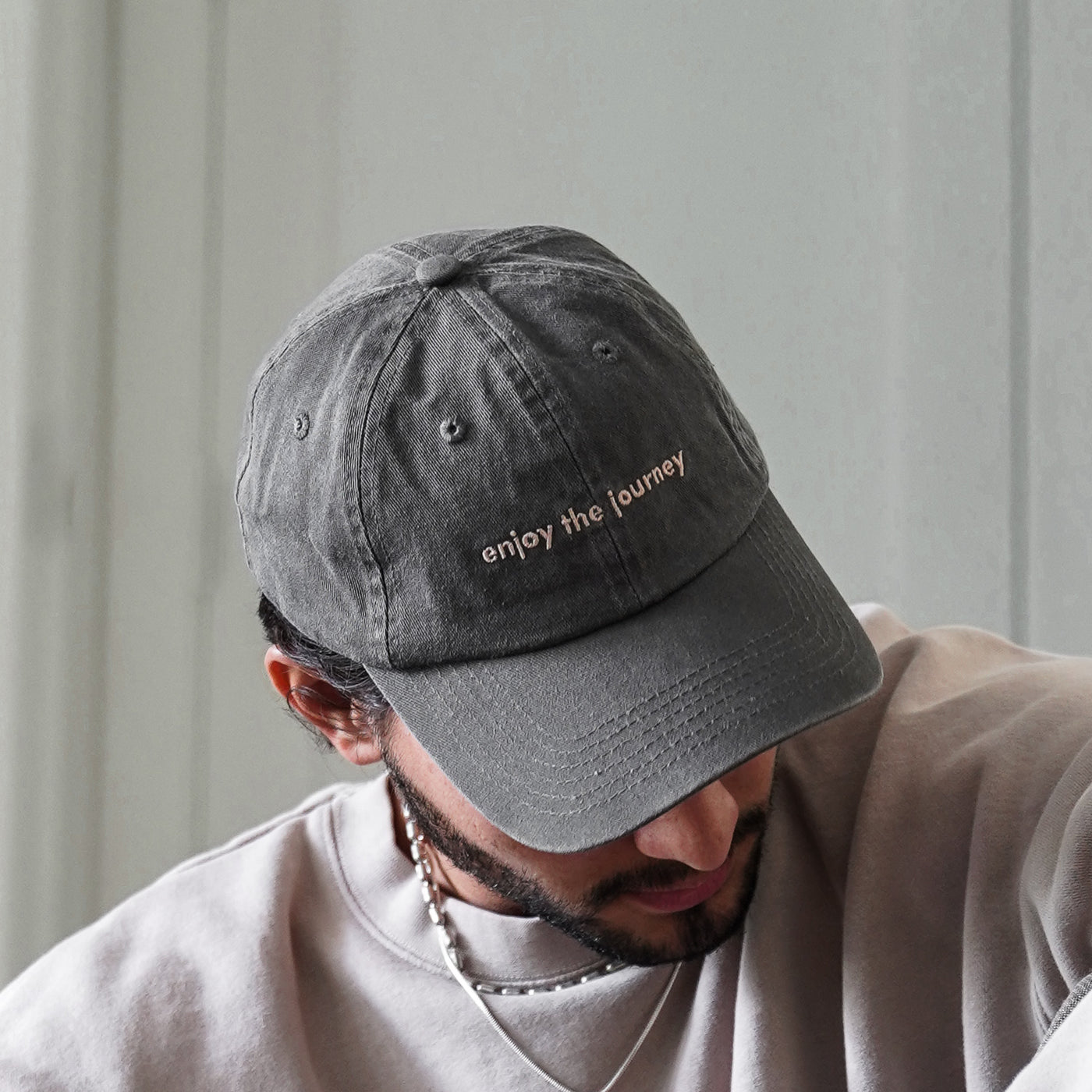 A person wearing a grey hat with the text 'enjoy the journey'.