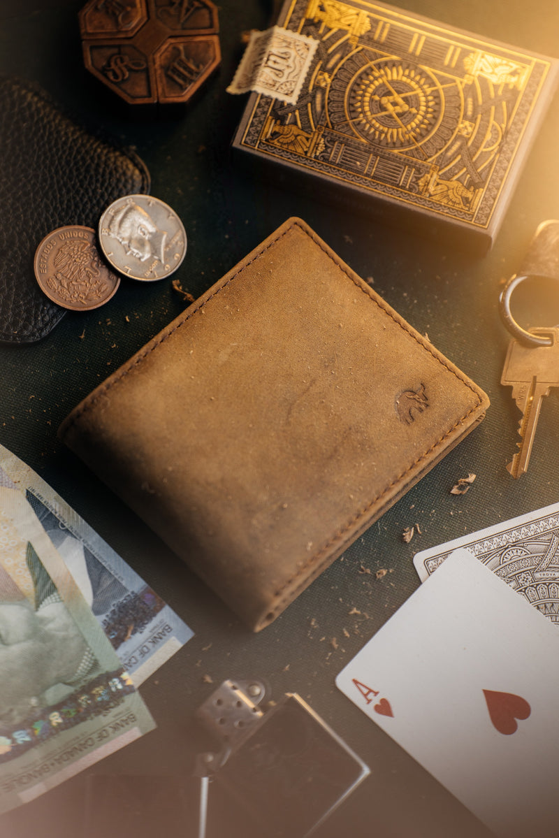 Angled top view of Terra bifold wallet showing worn brown leather and slim profile with coins, Ace of hearts playing card, keys, and banknotes nearby