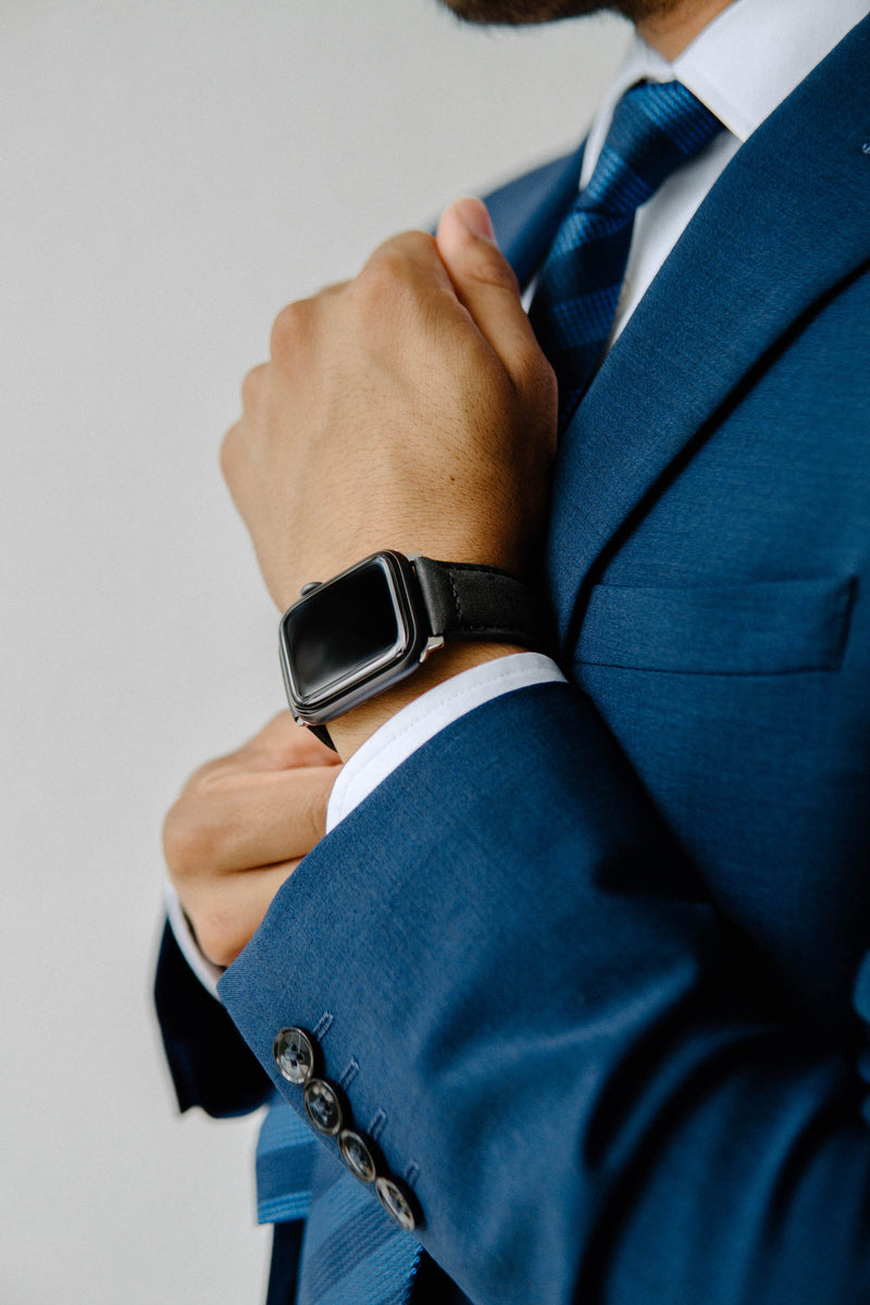 A person in a blue suit adjusting their cuff while wearing a black watch.