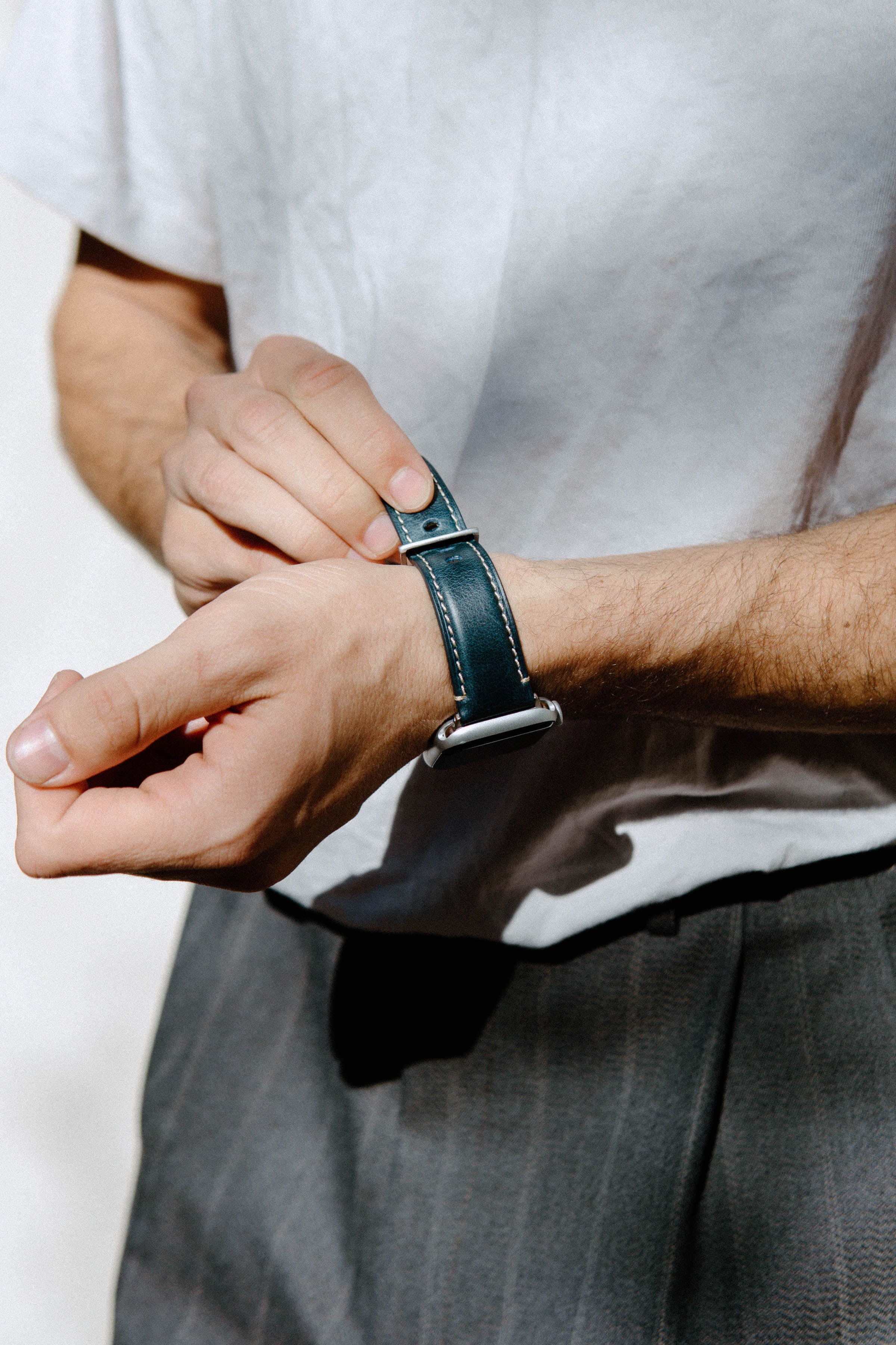 Person fastening a teal leather watch strap on their wrist, close-up of hands and watch band