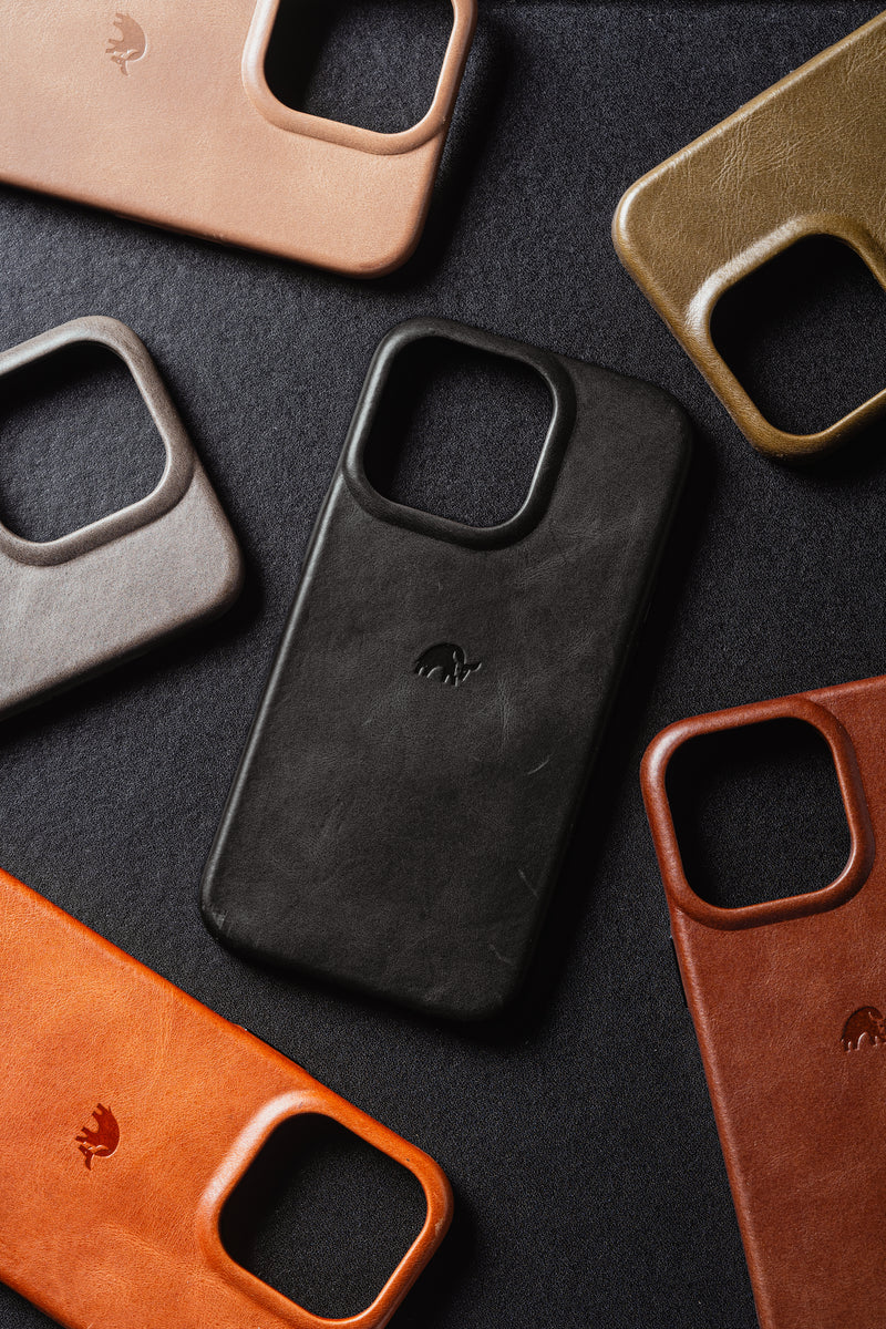 Leather smartphone cases in black, tan, brown, orange and gray arranged on a dark textured background