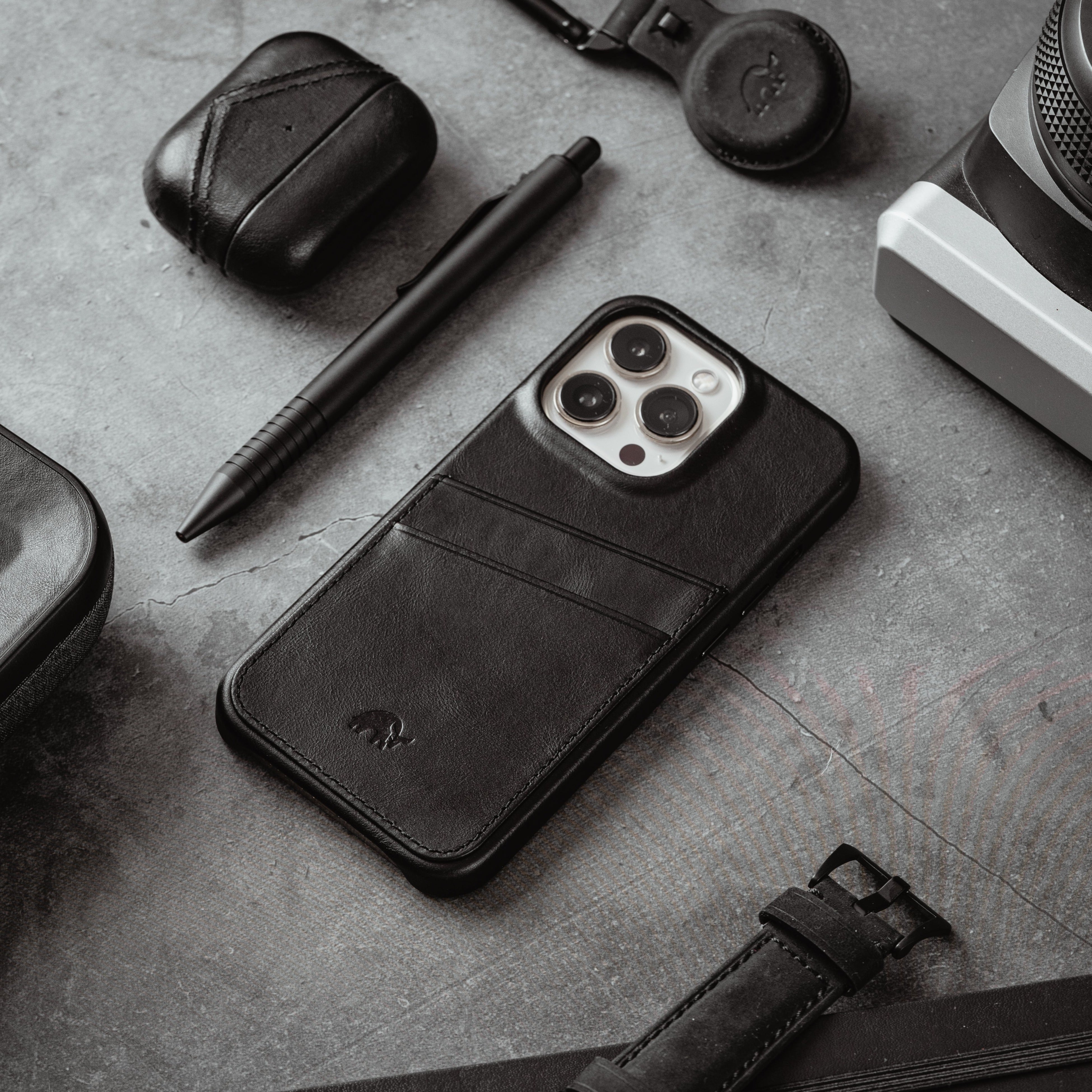 The Minimalist Portfolio Case in black, featuring a sleek design with card slots, placed on a textured surface with accessories.