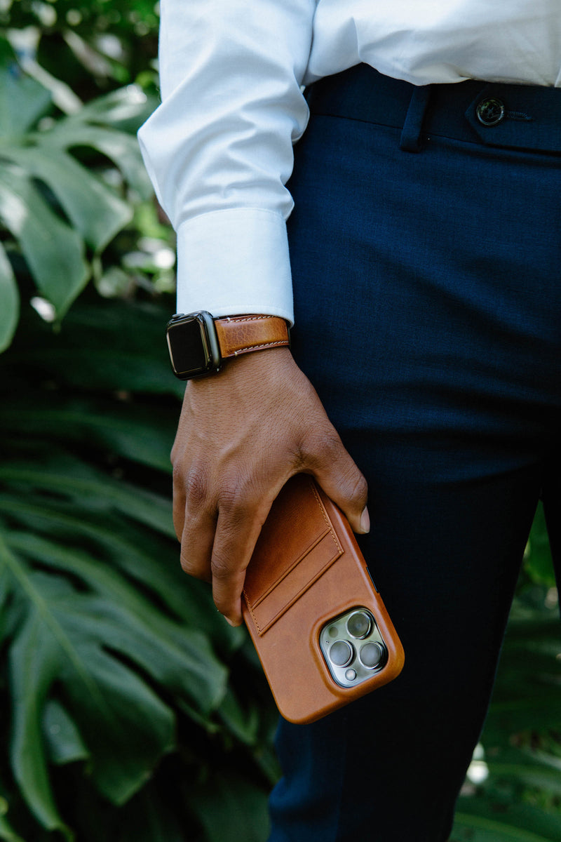 A person in a suit holding a brown leather phone case and wearing a watch.