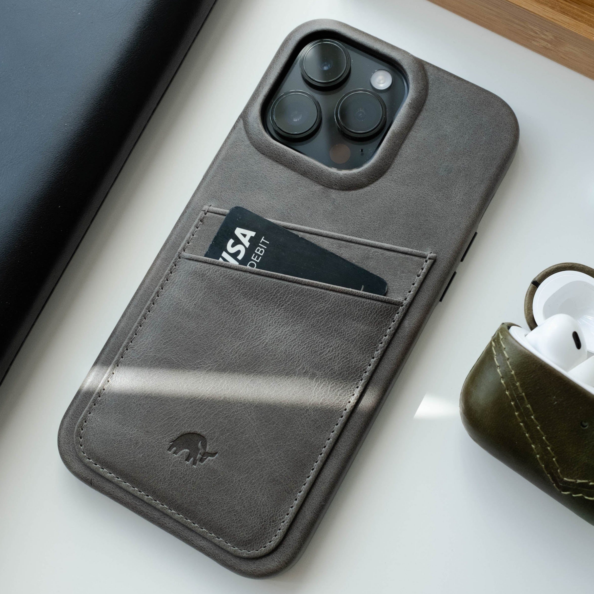 The Minimalist Portfolio Case in Slate color on a white surface next to AirPods
