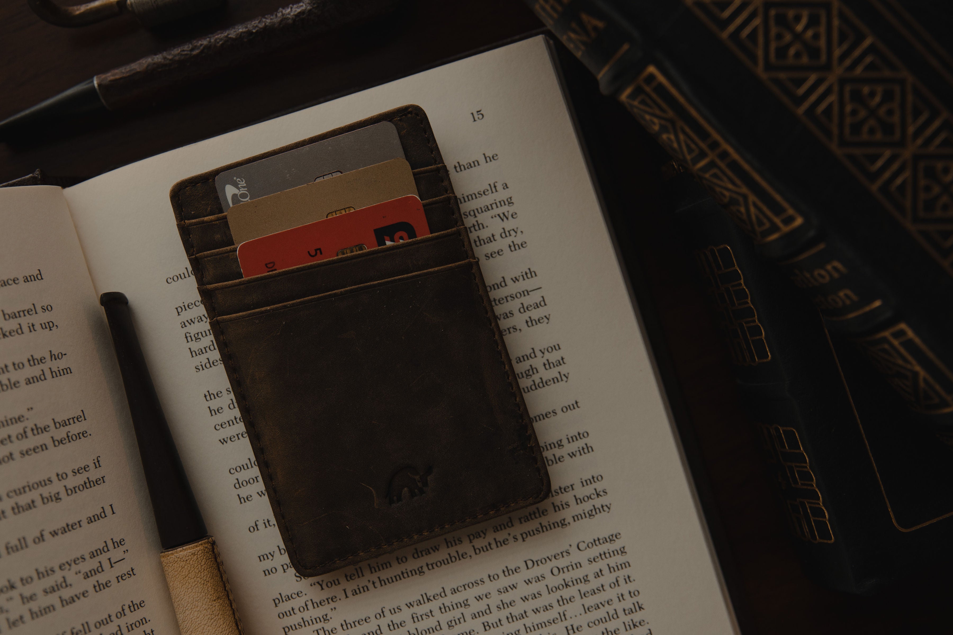 Brown leather card wallet on open book (page 15), three cards visible: gray 'One', gold, red '5', pen at left