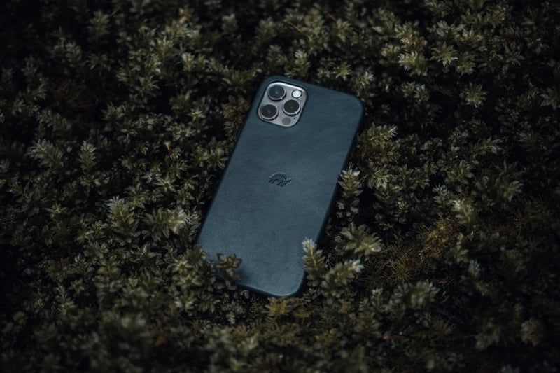 Angled view of Ocean leather iPhone case showcasing embossed bull logo and camera cutout on mossy forest floor