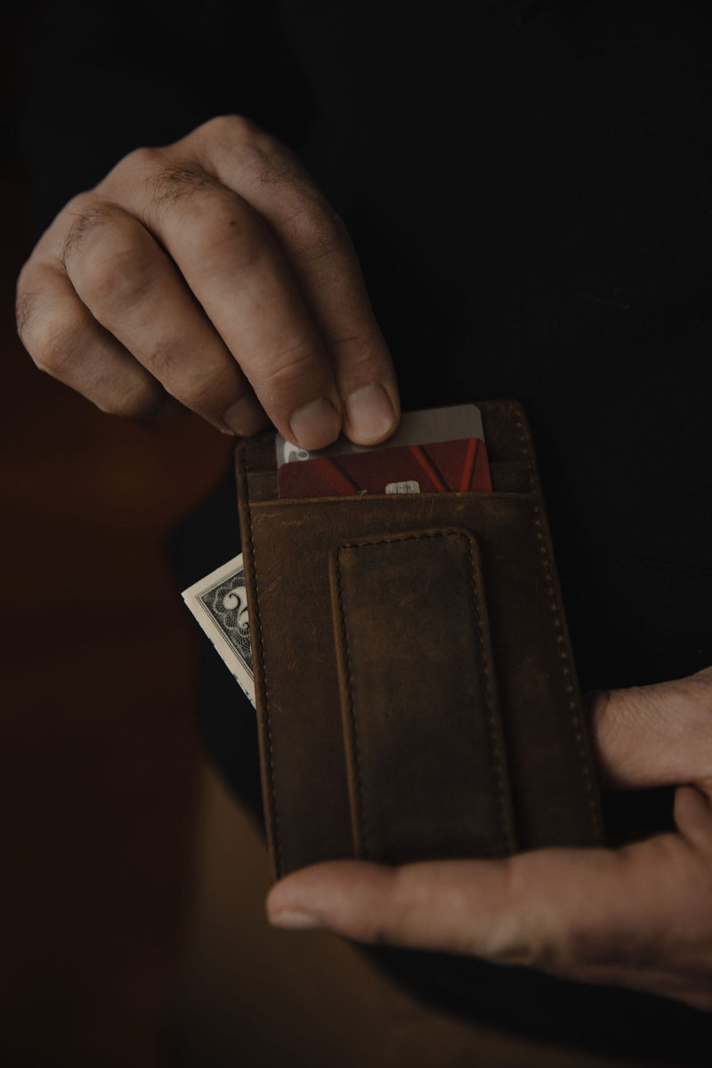 Close-up of hands holding Terra brown leather money-clip wallet showcasing cards in the top slot and cash in the external money clip