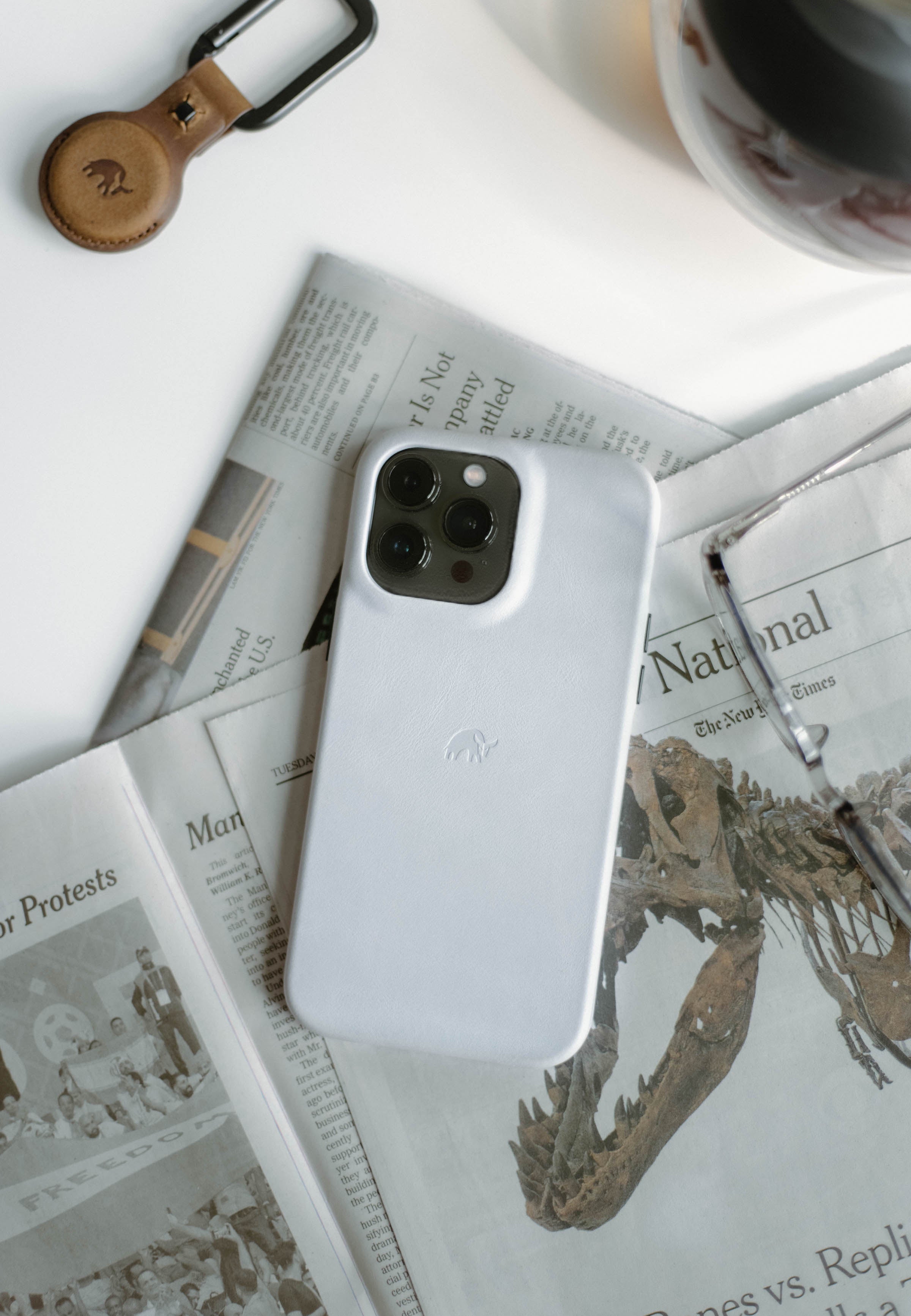 White leather iPhone on folded newspapers — National; The New York Times; Protests; FREEDOM — glasses and leather key fob.