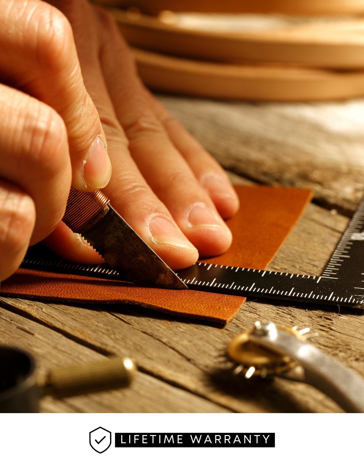 Hands cutting leather with craft knife along ruler on wooden workbench; LIFETIME WARRANTY label visible at bottom