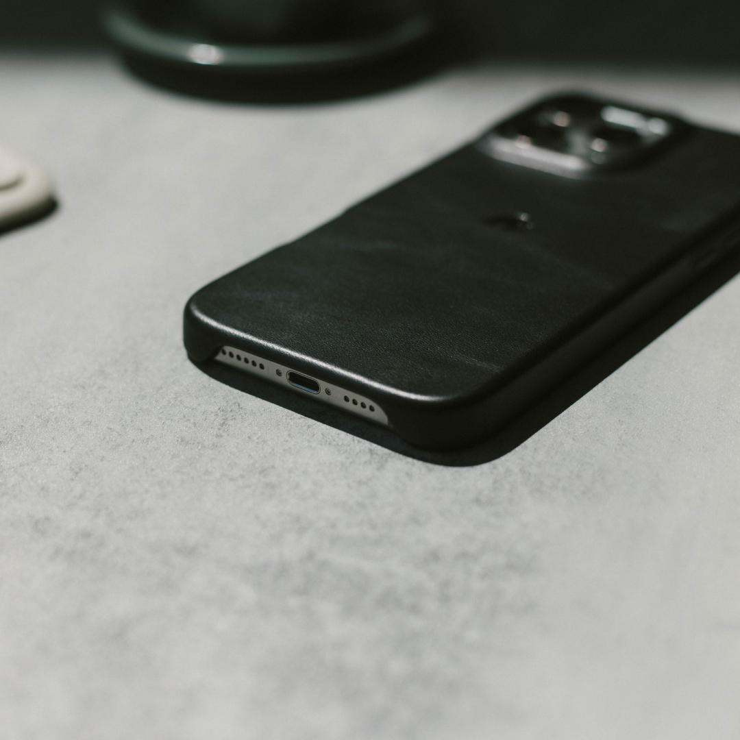 Slim black phone case on a gray tabletop, angled view showing back and bottom charging port cutout
