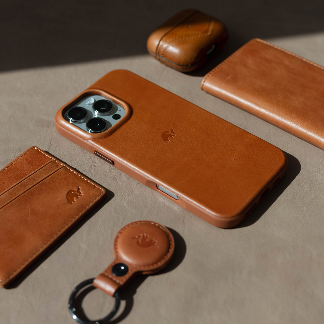 A brown leather iPhone case, wallet, and accessories on a beige surface.