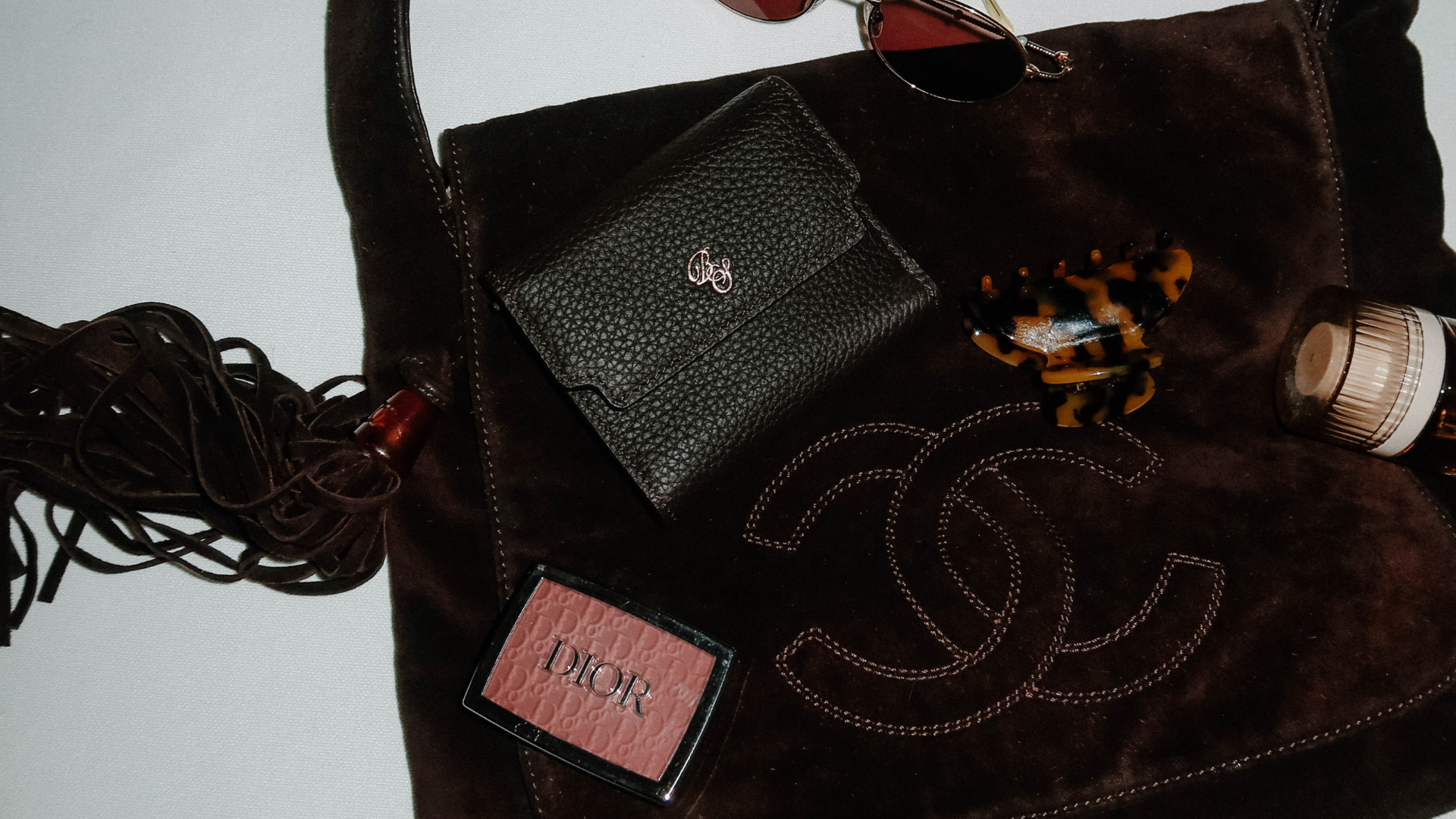 Brown suede Chanel bag with stitched double-C logo, black leather wallet, tortoiseshell hair clip, DIOR compact and sunglasses