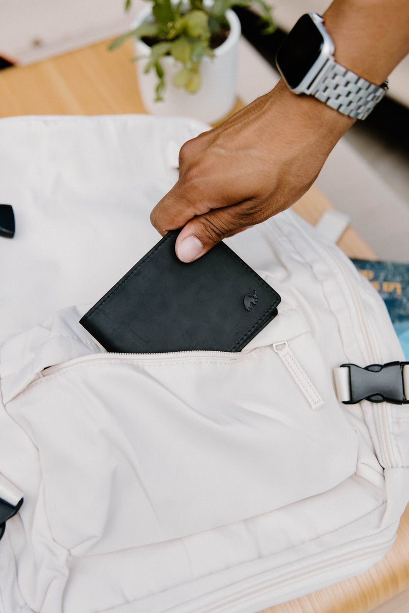 A hand placing a black bifold wallet into a white bag.