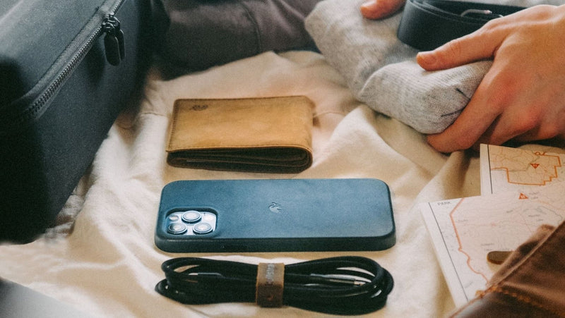 A flat lay of a phone case, wallet, charging cable, and folded clothes on a surface.