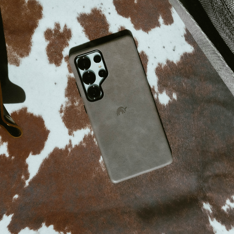 Smartphone with brown leather case and multiple rear cameras lying on a brown-and-white cowhide rug.