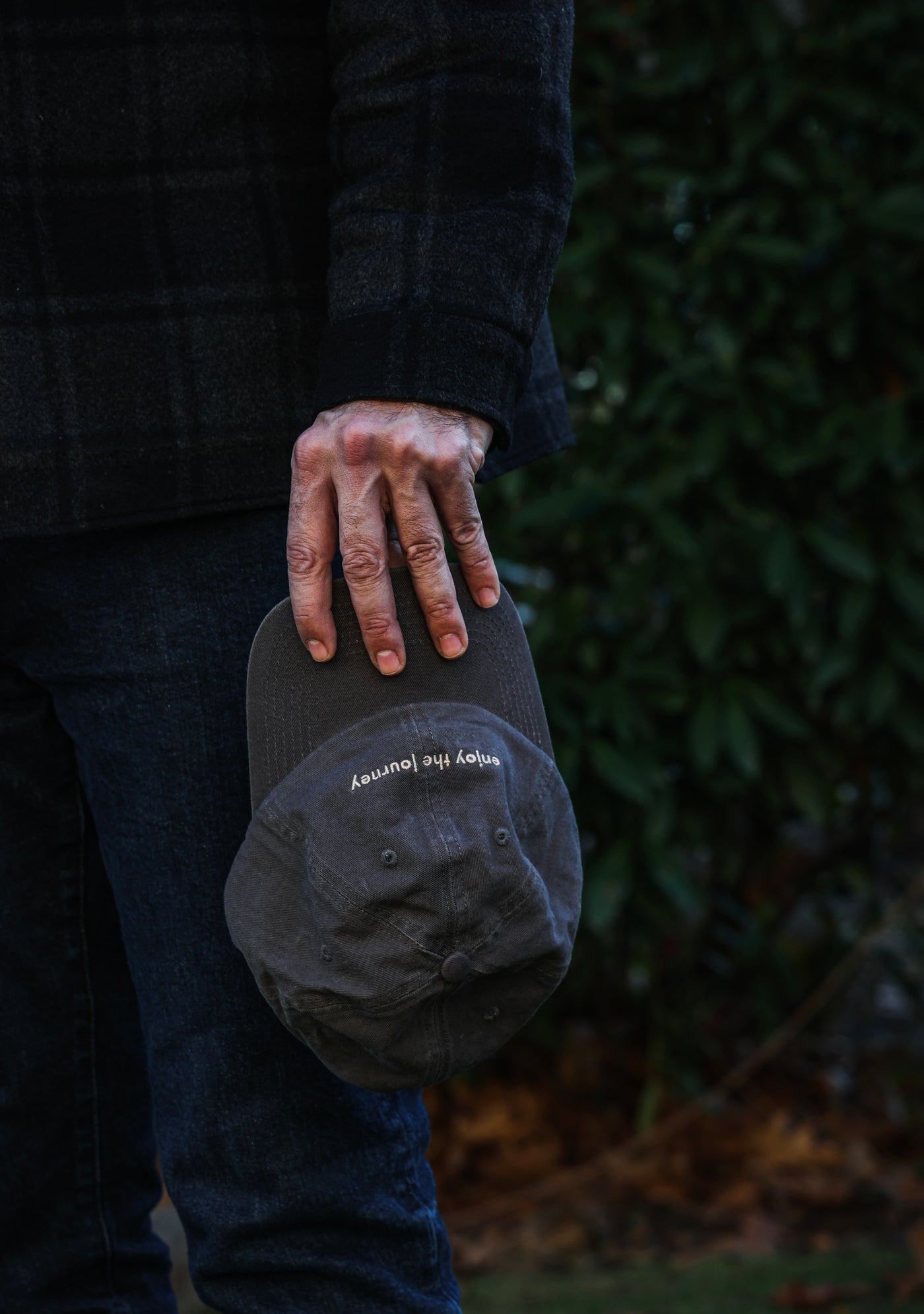A person holding a grey hat that says 'Enjoy the Journey'.