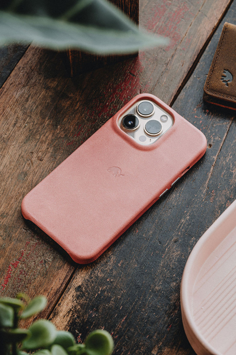 Pink leather iPhone case face down on a worn wooden table showing the camera lenses