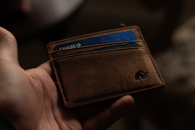 A hand holding a brown leather wallet with a Chase card visible in the slots.