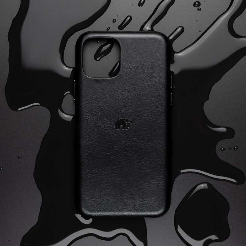 Top view of black leather iPhone case showing full-grain texture and embossed bull logo on black surface with spilled liquid
