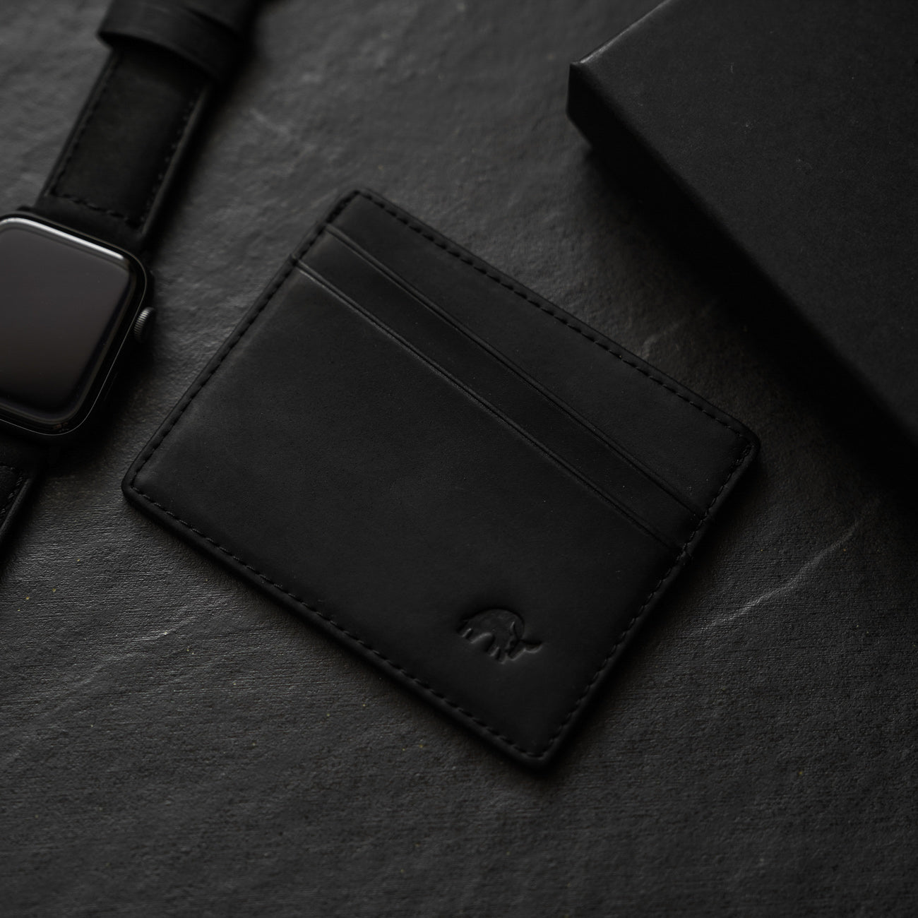 Black leather card holder with three card slots on a dark surface
