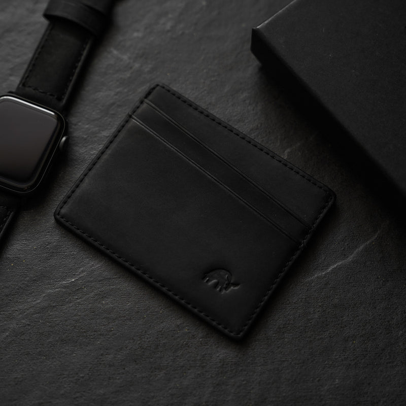 Black leather card holder with three card slots on a dark surface