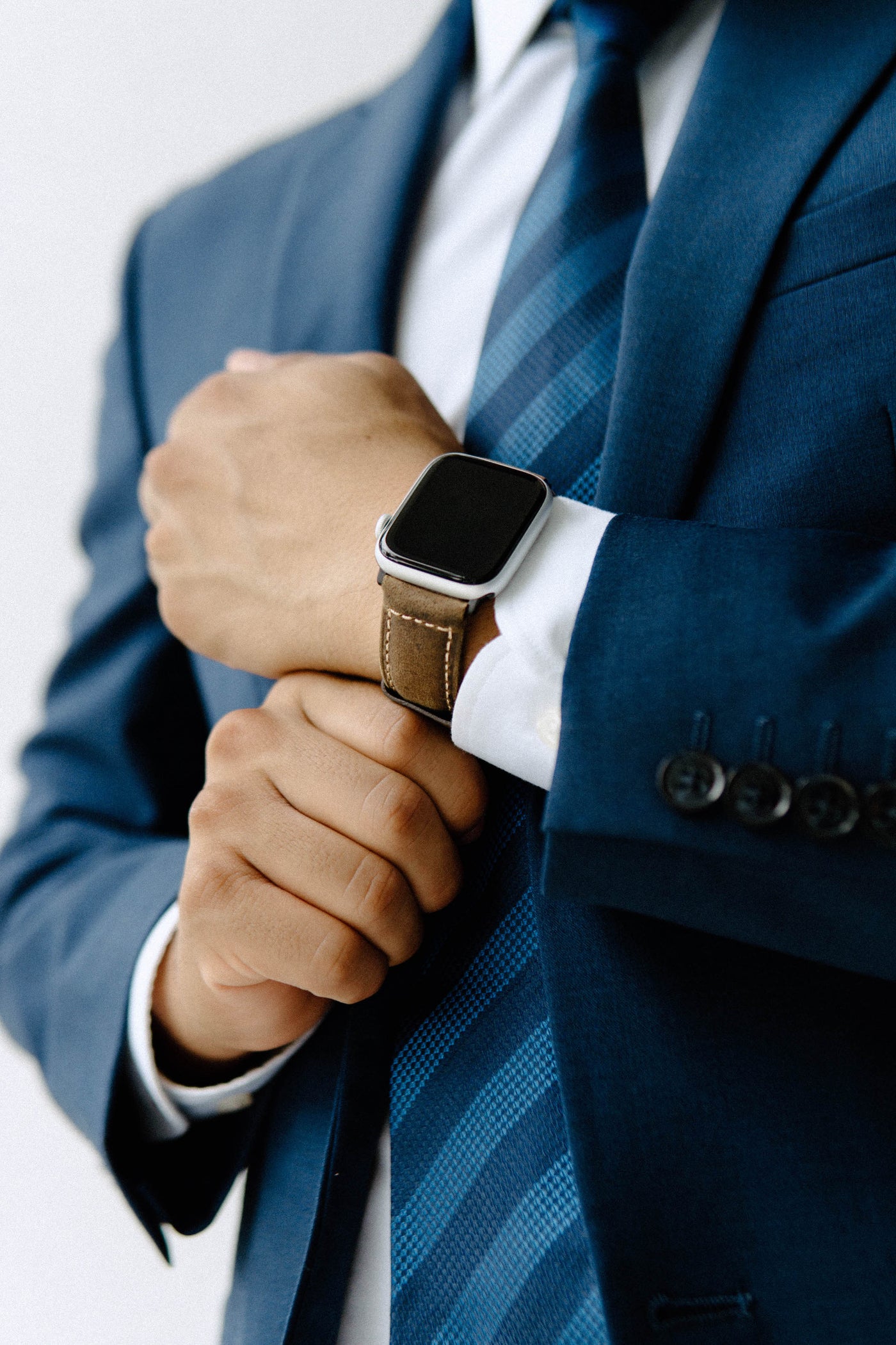 A person in a blue suit adjusting their watch with a leather strap.