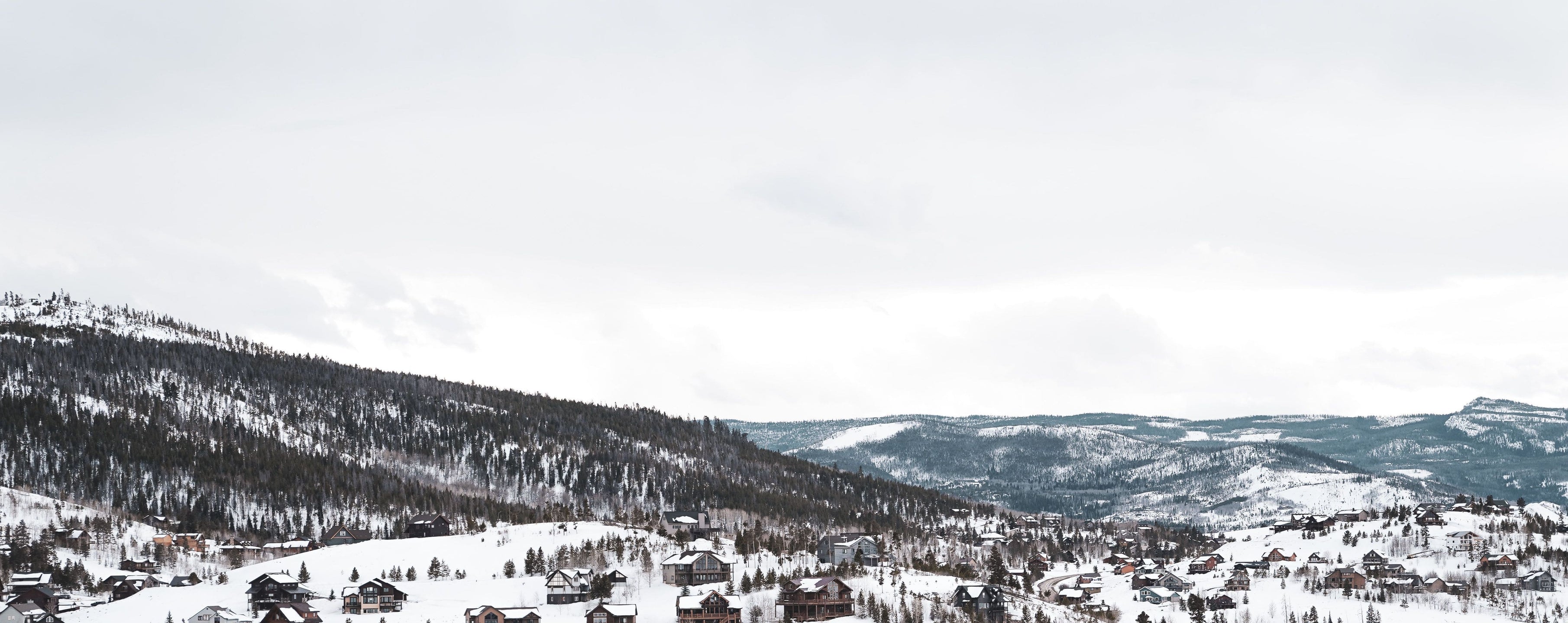 A panoramic view of a snowy landscape with houses in a mountainous area.