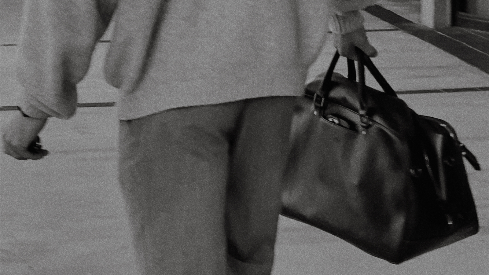 A person walking while carrying a black leather bag.