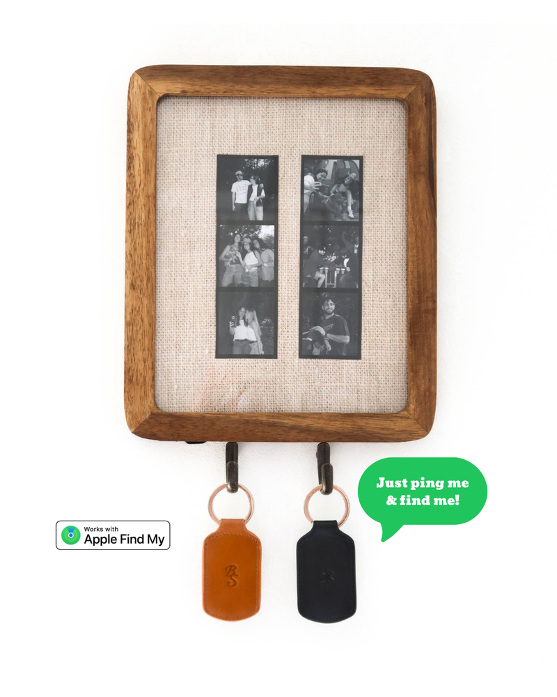 Front view of Trace trackable keychains in sienna and black showcasing Apple Find My badge, hanging from a wooden frame