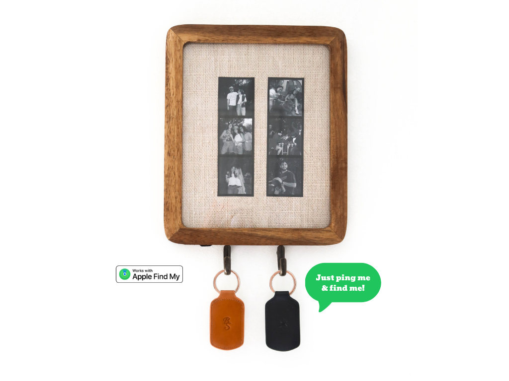 Front view of Trace trackable keychains in sienna and black showcasing Apple Find My badge, hanging from a wooden frame