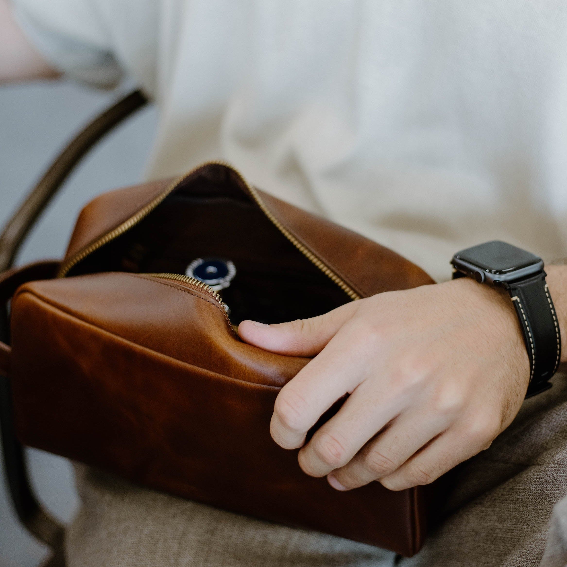 A person holding a brown leather toiletry bag with an open zipper, revealing its interior.
