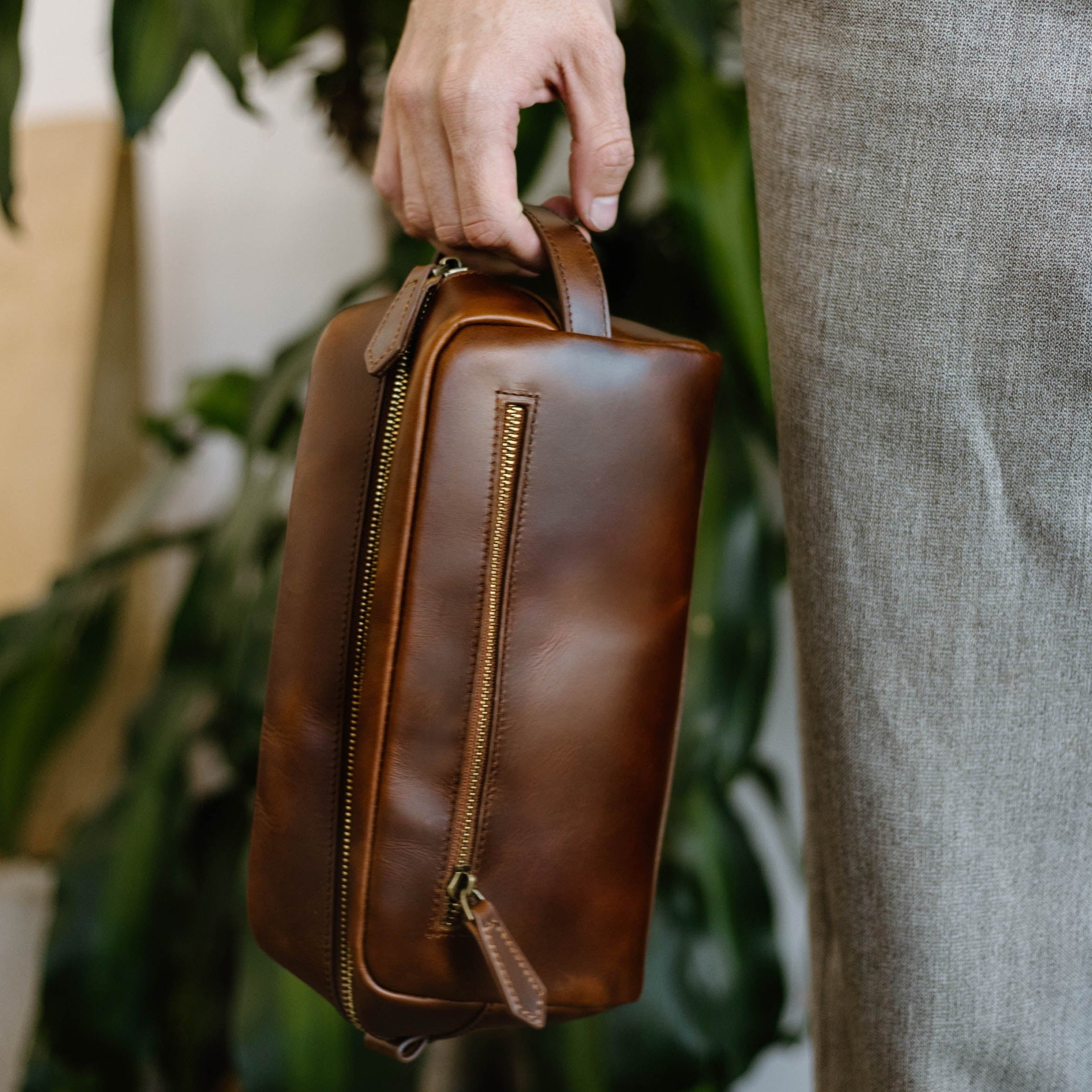 A person holding a brown leather travel bag with a zipper.