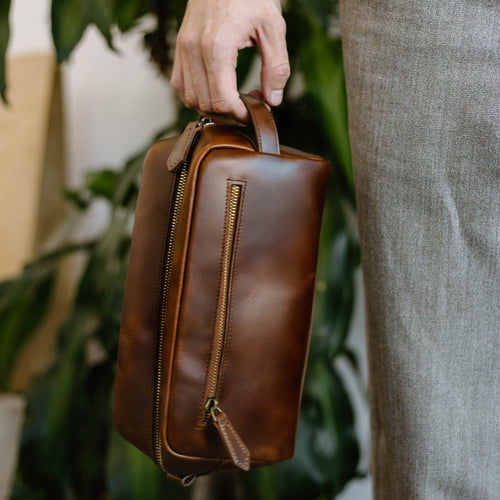 A person holding a brown leather travel bag with a zipper.