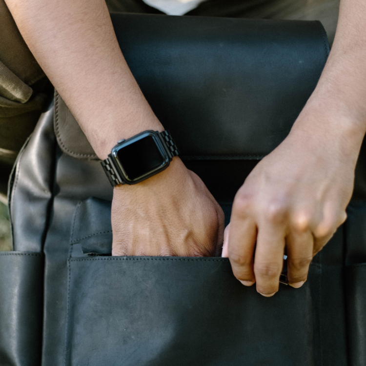 Black metal link Apple Watch strap worn on wrist reaching into a black leather bag